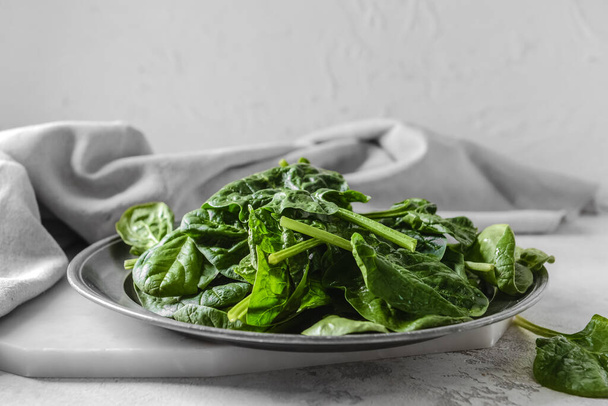 Plate with fresh spinach leaves on light background - Foto, afbeelding