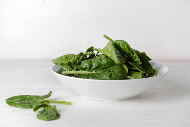 Bowl with fresh spinach leaves on light wooden background - Photo, Image
