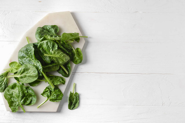 Board with fresh spinach leaves on light wooden background - Photo, Image