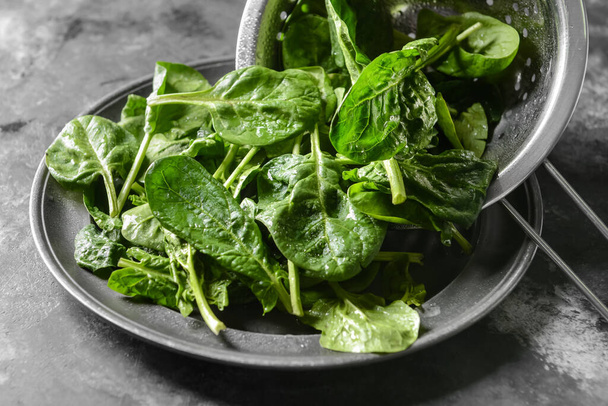 Colino e piatto con foglie di spinaci freschi su fondo grigio, primo piano - Foto, immagini