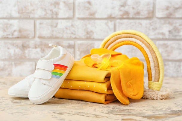 Набір дитячого одягу, взуття та іграшок на столі проти цегляної стіни
 - Фото, зображення