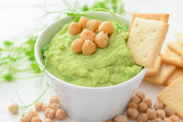 Bowl with tasty green pea hummus, chickpeas and crackers on light background, closeup - Photo, Image