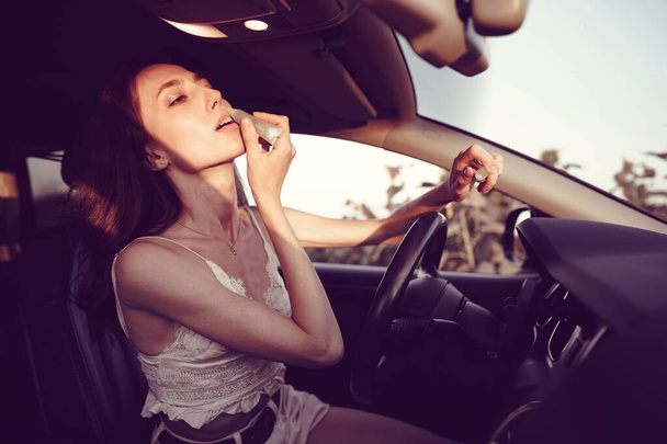 Beautiful young caucasian woman painting lips on the front seat of her car - 写真・画像