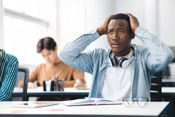 Black male student grabbing head sitting at desk in class - Photo, Image