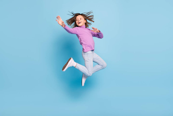Photo of funny adorable small schoolgirl dressed violet turtleneck smiling jumping high isolated blue color background - Foto, Imagem