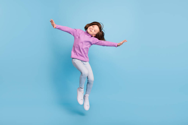 Photo of pretty charming school girl wear purple turtleneck jumping high smiling isolated blue color background - Foto, Imagen