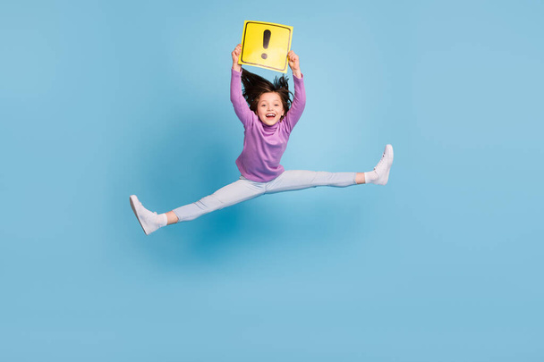 Photo of charming cute school girl wear purple turtleneck jumping high holding attention card smiling isolated blue color background - Foto, afbeelding