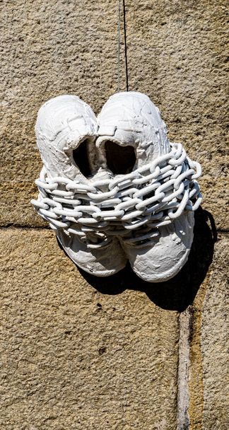 Eine angekettete weiße Schuhskulptur hängt an der Wand. Freiheit, Ketten, weiß. - Foto, Bild