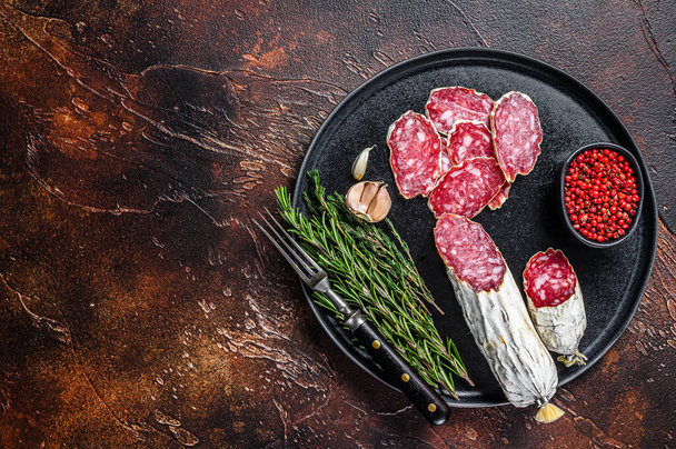 Italian sliced salami on a plate with rosemary and thyme. Dark background. Top view. Copy space - Fotografie, Obrázek