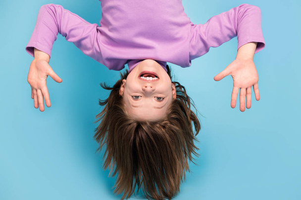 Portrait photo little girl hanging upside down laughing overjoyed isolated pastel blue color background - 写真・画像