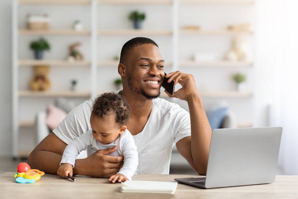 Чорний робочий батько розмовляє на мобільному телефоні під час няні дитини вдома
 - Фото, зображення