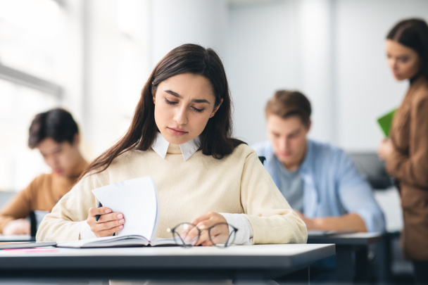 Vrouwelijke student zit aan een bureau in de klas schrijven examen - Foto, afbeelding