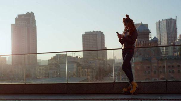 Стильна жінка використовує телефон на вулиці. Красива дівчина дивиться на мобільний телефон на відкритому повітрі
. - Фото, зображення
