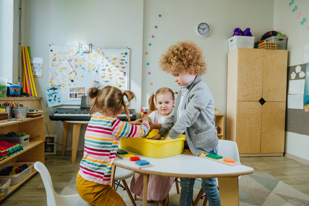 Preschool students playing with raw mung beans in a container. Learning play activities in kindergarten or daycare centre. Education concept. Selective focus. - 写真・画像