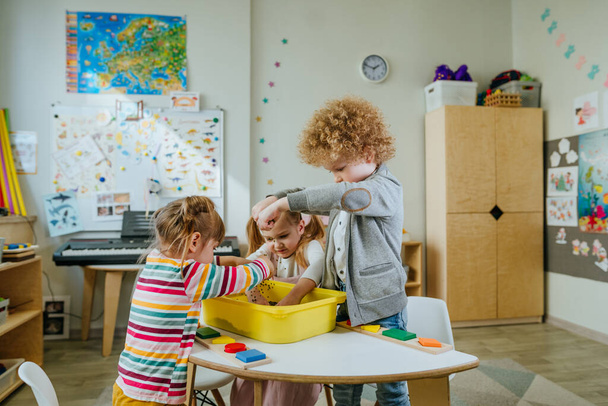 Preschool students playing with raw mung beans in a container. Learning play activities in kindergarten or daycare centre. Education concept. Selective focus. - 写真・画像