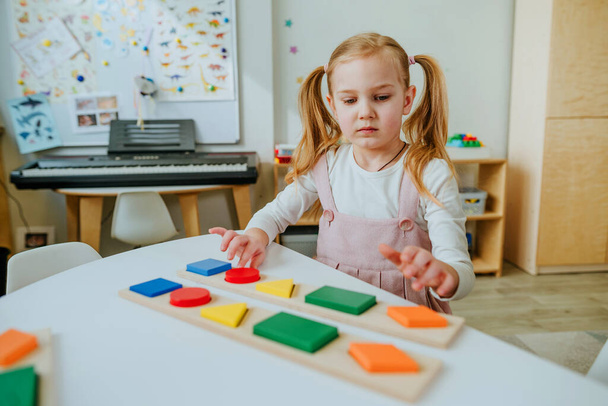 Adorable preschool student sorting wooden geometric forms. Learning play activities in kindergarten or daycare centre. Education concept. Selective focus. - 写真・画像