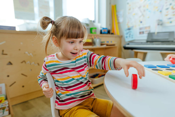 Adorable preschool student sorting wooden geometric forms. Learning play activities in kindergarten or daycare centre. Education concept. Selective focus. - Photo, Image