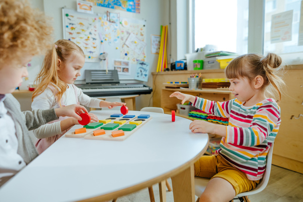 Preschool students sorting wooden geometric forms. Learning play activities in kindergarten or daycare centre. Education concept. Selective focus. - 写真・画像