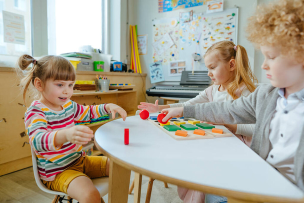 Preschool students sorting wooden geometric forms. Learning play activities in kindergarten or daycare centre. Education concept. Selective focus. - Photo, Image