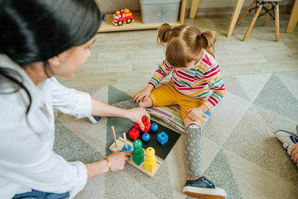 Дошкільнята сортують дерев'яні геометричні іграшкові кульки та кубики, що сидять на підлозі. Навчання іграшок в дитячому або денному садочку. Концепція освіти. Вибірковий фокус
. - Фото, зображення