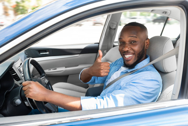 Gelukkige zwarte man zit in auto gebaren duimen omhoog - Foto, afbeelding