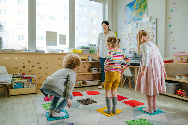 Kid's physical activities and fun games in kindergarten with orthopedic massage mats for legs that incorporate training for balance, strength, coordination and endurance. - Foto, Bild