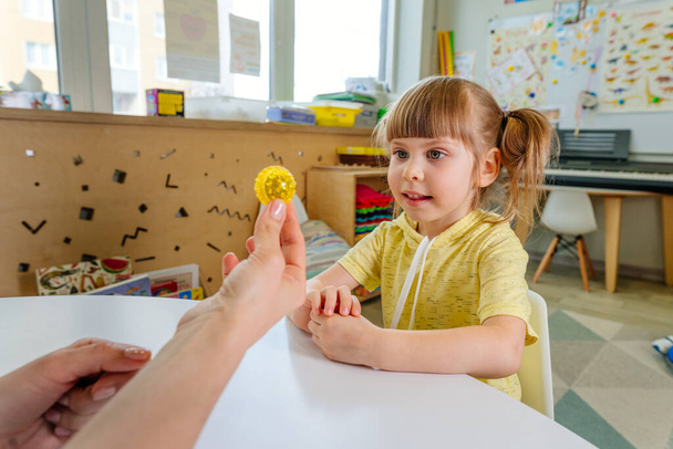幼稚園での運動技術の発達の教訓についての小さな女の子。幼児の感覚認識能力や発話能力を高める活動として指マッサージで遊ぶ. - 写真・画像