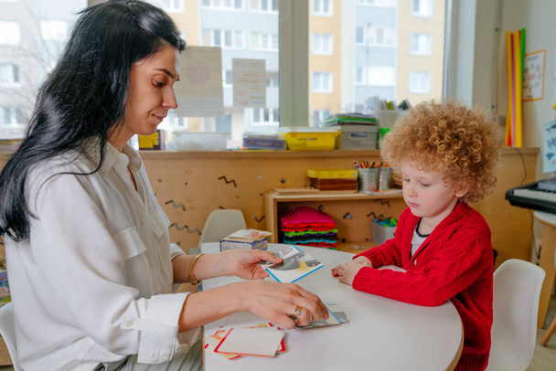 Boy on the session of speech therapist. Lesson on the development of speech in kindergarten. Teacher spreads out puzzle in front of the child. - Photo, image