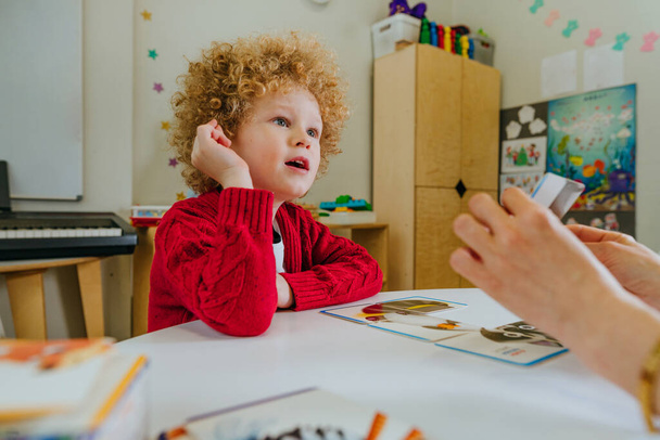 Boy on the session of speech therapist. Lesson on the development of speech in kindergarten. Teacher spreads out puzzle in front of the child. - Photo, Image