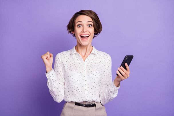 Portrait of nice brunette short hairdo hooray lady hold telephone wear white shirt isolated on lilac color background - Φωτογραφία, εικόνα