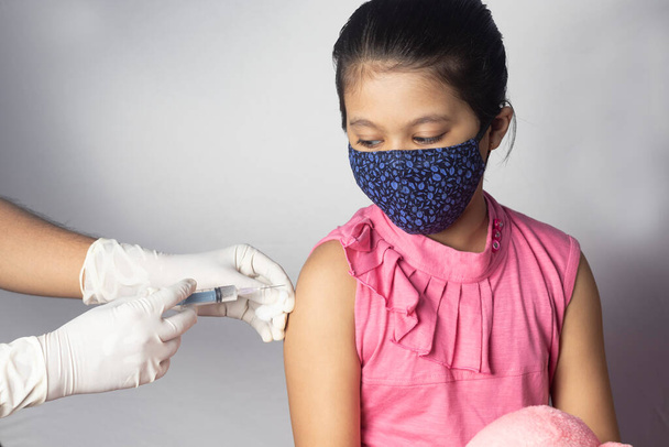Una bambina indiana in maschera nasale che riceve una dose di vaccino su sfondo bianco - Foto, immagini