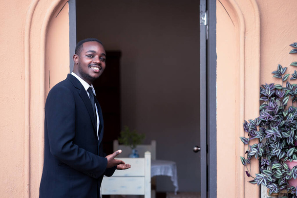 Il proprietario del ristorante e della caffetteria sta aprendo la porta, invitando i clienti al suo negozio.Uomo d'affari africano in piedi e sorridente - Foto, immagini