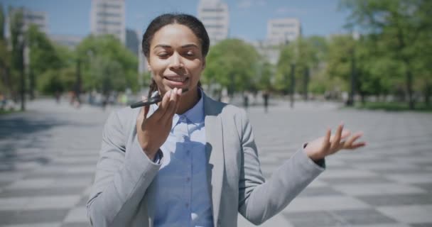 Comunicación de audio. Joven afro-americana ocupada jefa grabando mensaje de voz a su asistente, yendo al parque - Metraje, vídeo