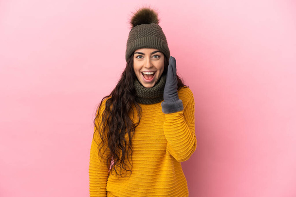 Young caucasian girl with winter hat isolated on purple background with surprise and shocked facial expression - Foto, imagen