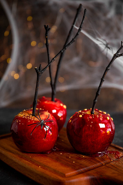  Red apples in caramel with a festive Halloween decor, an original treat for a festive Halloween table decorated with spiders and cobwebs, photo vertical - Photo, Image