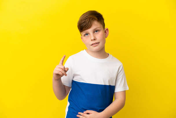Little redhead boy isolated on yellow background pointing up a great idea - Fotografie, Obrázek