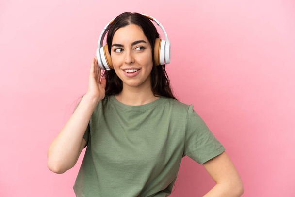 Junge kaukasische Frau isoliert auf rosa Hintergrund Musik hören - Foto, Bild