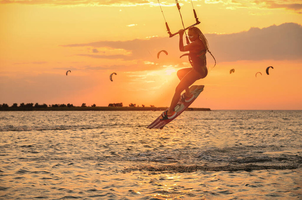 Young woman professional kiter performs a difficult trick in the air on a beautiful background of the sunset and sea - Foto, imagen