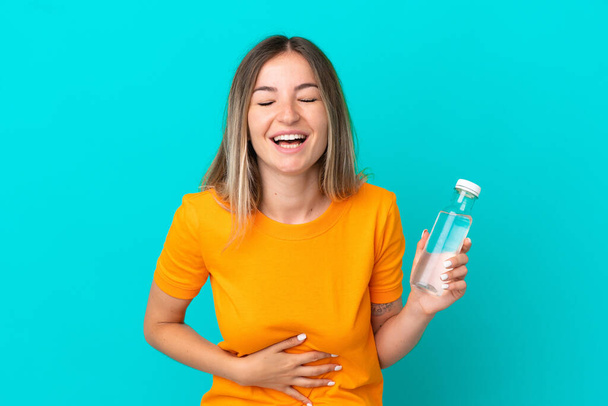 Mladá rumunská žena s lahví vody izolované na modrém pozadí s úsměvem hodně - Fotografie, Obrázek