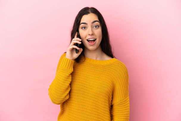 Mujer joven caucásica usando teléfono móvil aislado sobre fondo rosa con expresión facial sorpresa - Foto, imagen