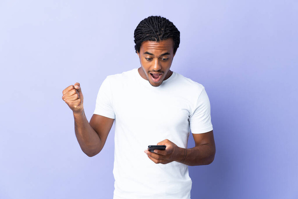 Young African American man with braids man isolated on purple background surprised and sending a message - Photo, Image