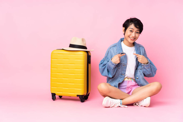 Young traveler Vietnamese woman with suitcase sitting on the floor over isolated pink background with surprise facial expression - 写真・画像