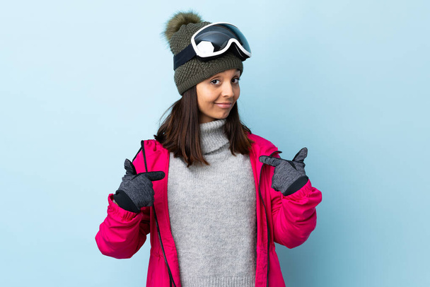 Змішана гоночна лижниця дівчина зі сноубордистськими окулярами над ізольованим синім тлом пишається і самозадоволена
. - Фото, зображення