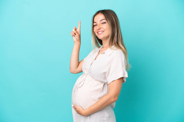 Junge Rumänin isoliert auf blauem Hintergrund schwanger und zeigt nach oben - Foto, Bild