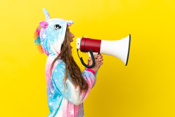 Κορίτσι με πυτζάμες μονόκερου πάνω από απομονωμένο φόντο φωνάζοντας μέσα από ένα μεγάφωνο - Φωτογραφία, εικόνα