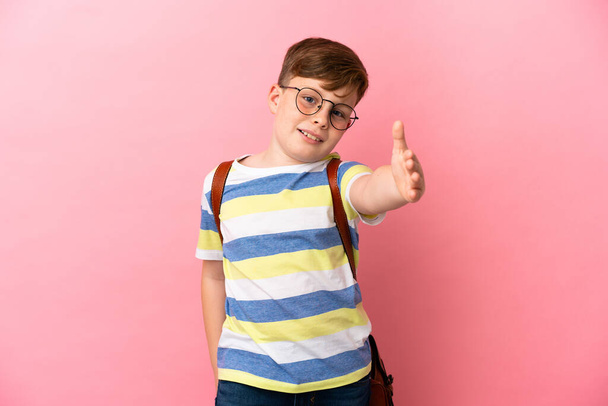 Little redhead caucasian boy isolated on pink background shaking hands for closing a good deal - Foto, Bild