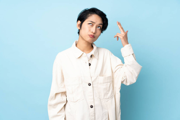 Young Vietnamese woman with short hair over isolated background with problems making suicide gesture - Photo, Image