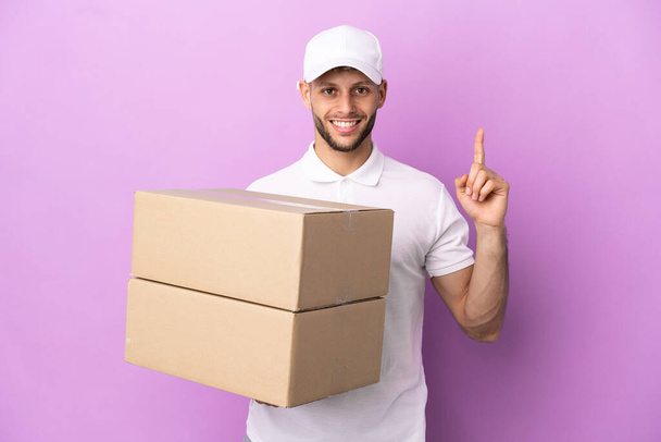 Delivery caucasian man isolated on purple background pointing up a great idea - Photo, Image