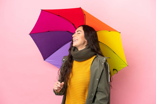 Молода жінка тримає парасольку ізольовано на рожевому фоні, сміючись у бічному положенні
 - Фото, зображення