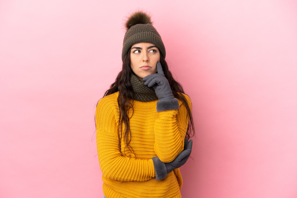 Young caucasian girl with winter hat isolated on purple background having doubts while looking up - 写真・画像
